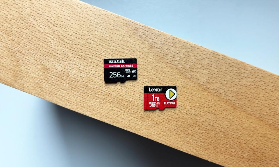 Two microSD cards, one mostly black and one mostly red, rest on top of a brown wooden stand above a white window ledge.