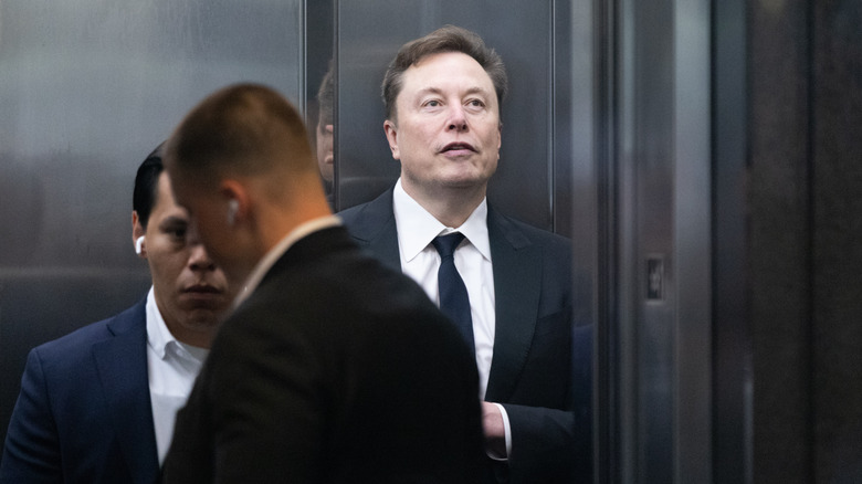 Elon Musk in an elevator with two men standing near him.