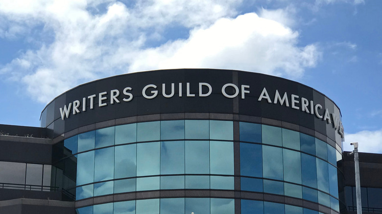Photo of the Writers Guild of America West offices. A rounded, windowed building captured below a blue sky with clouds.